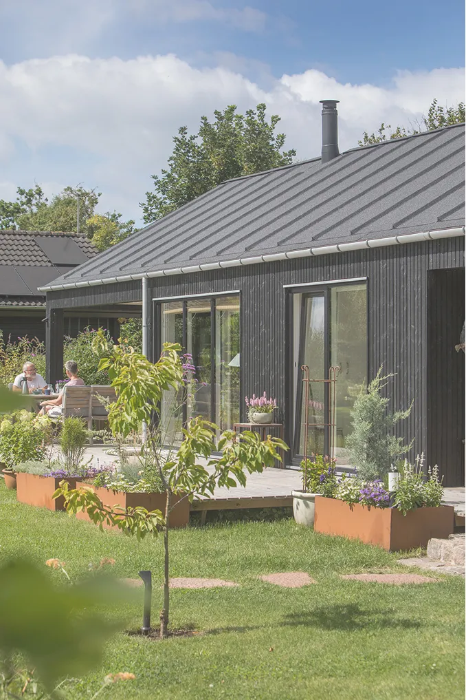 fjordhuset i sort, med en grøn, blomstrende have